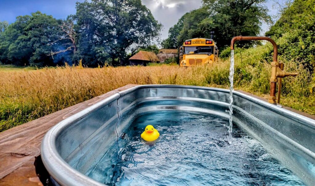 Quirky glamping hot tub with flowing tap and rubber duck, with retro yellow school bus in background at Skoolie Stays