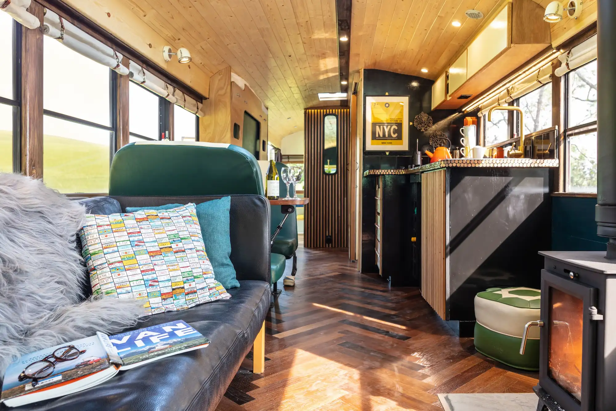 Cosy cabin-style interior of the Skoolie bus with sofa, kitchen and wood burner in West Sussex