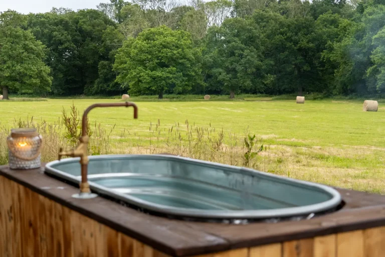 Wood-fired hot tub beside the Skoolie Stays glamping bus overlooking a quiet meadow in West Sussex