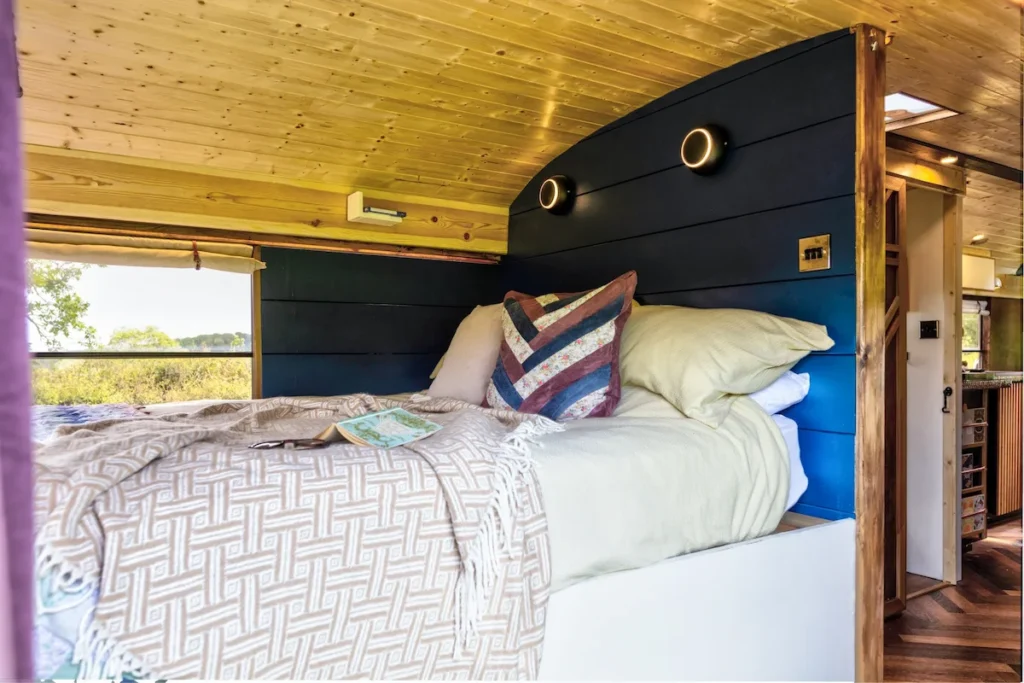 Cabin-style bedroom inside the Skoolie Stays glamping bus with king-size bed and countryside views in West Sussex