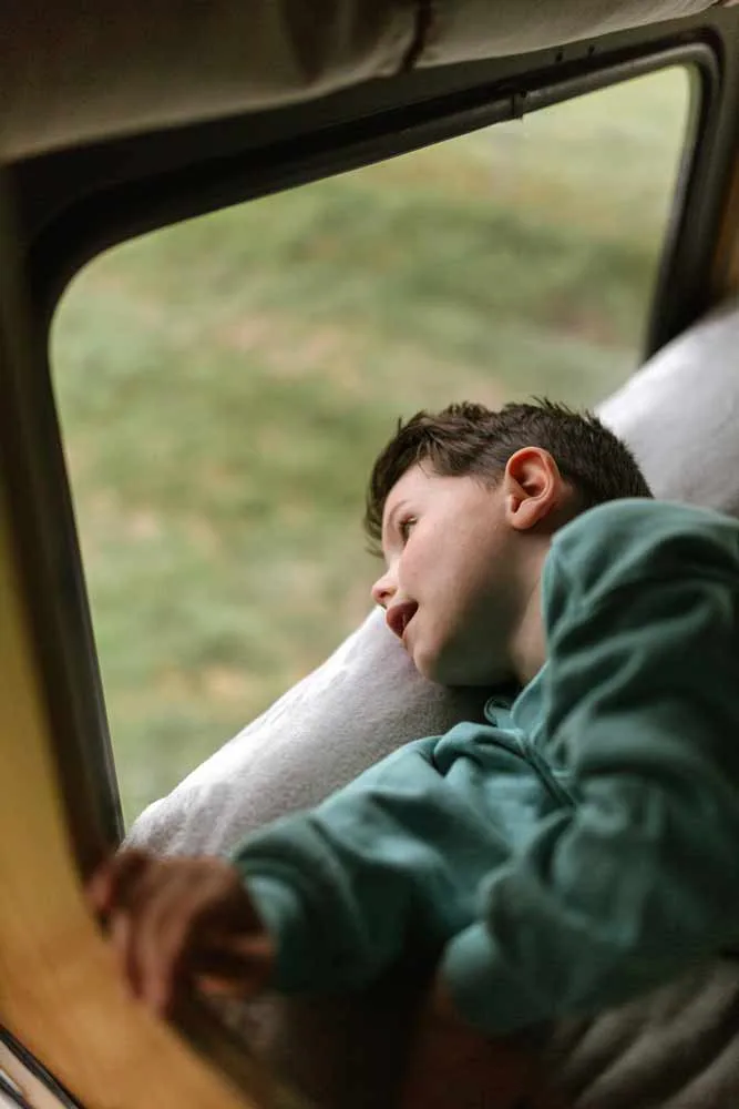 Child resting by the window inside a converted American school bus at Skoolie Stays
