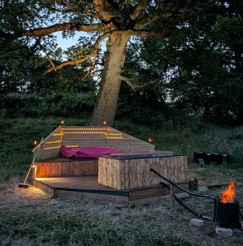 Private wood-fired hot tub beneath an oak tree at night in West Sussex
